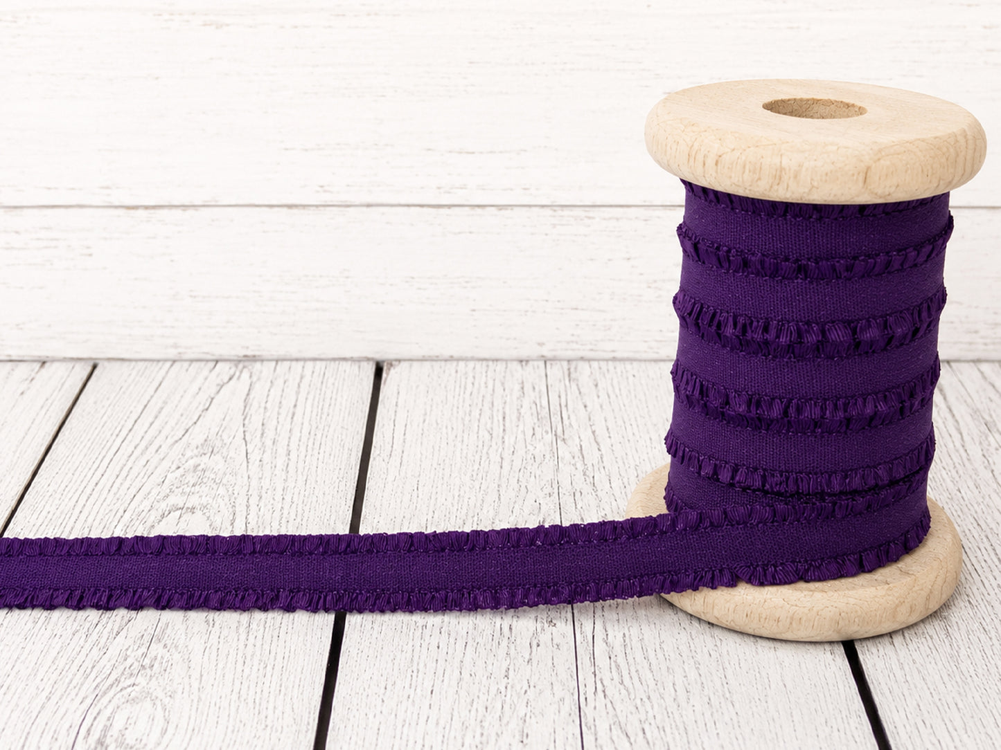 Violett Rüschen Gummiband auf einer Holzspule, ideal für Nähprojekte und Verzierungen.