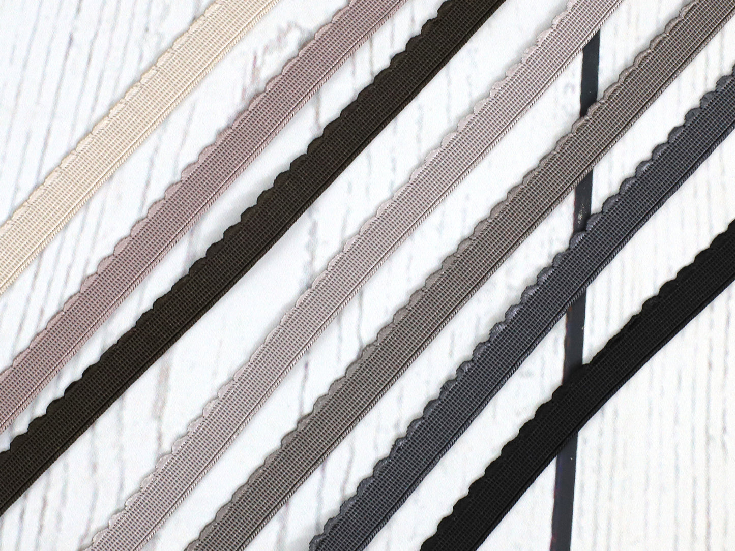 Schwarzes Gummiband mit Bogenkante 12mm in verschiedenen Farben auf einem hellen Holzuntergrund.