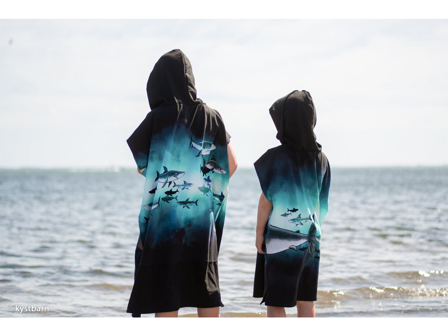 Two children wearing shark-themed hooded towels by the beach, showcasing the lively design and vibrant colors.
