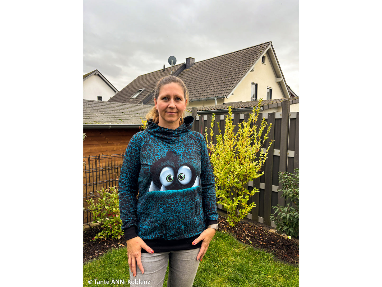 Woman wearing a hoodie made from French Terry fabric panel for sewing, featuring a playful design in a garden setting.