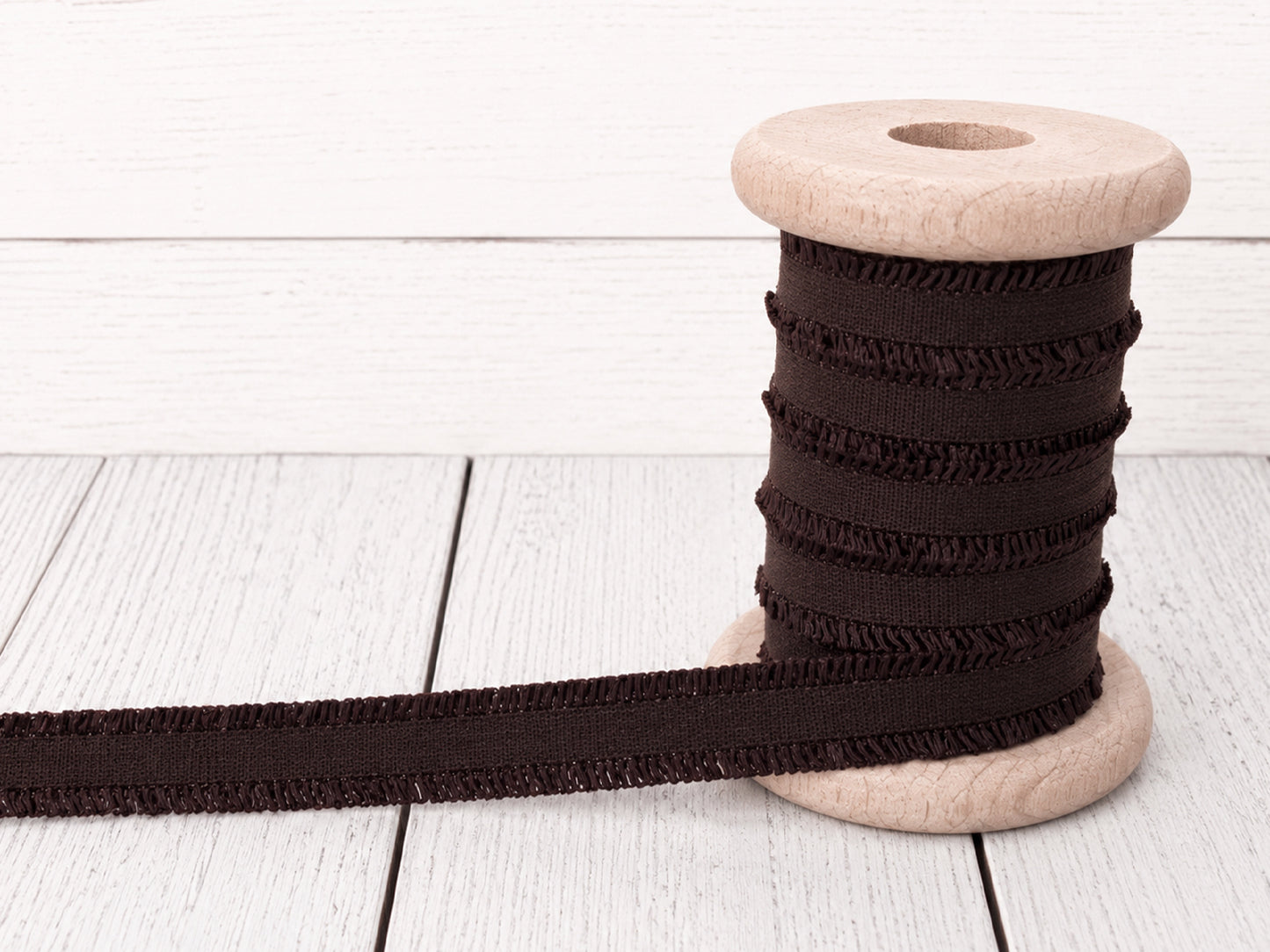 dunkelbraunes Rüschen Gummiband auf einer Holzspule, ideal für Nähprojekte und Bastelarbeiten.