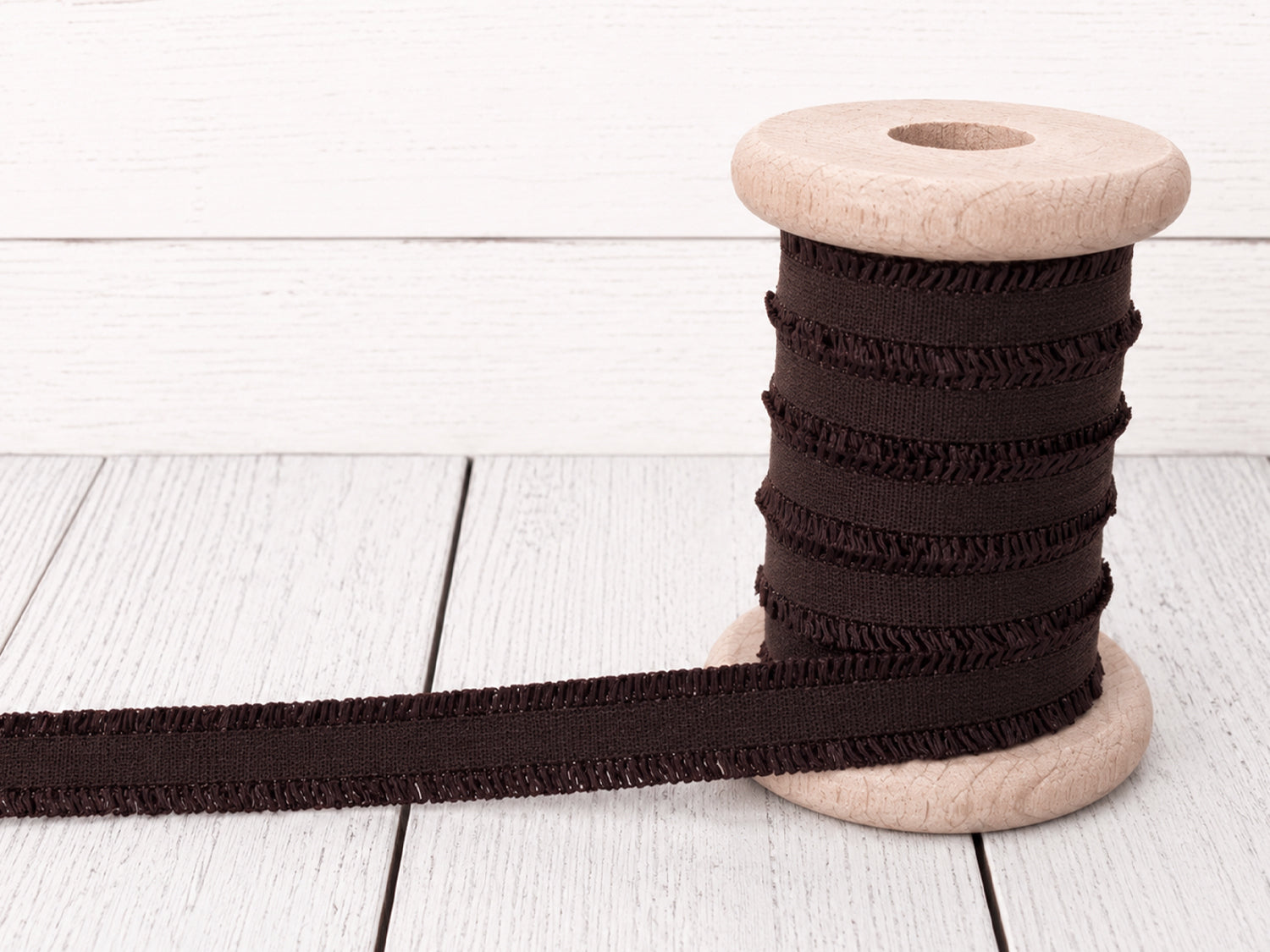 dunkelbraunes Rüschen Gummiband auf einer Holzspule, ideal für Nähprojekte und Bastelarbeiten.