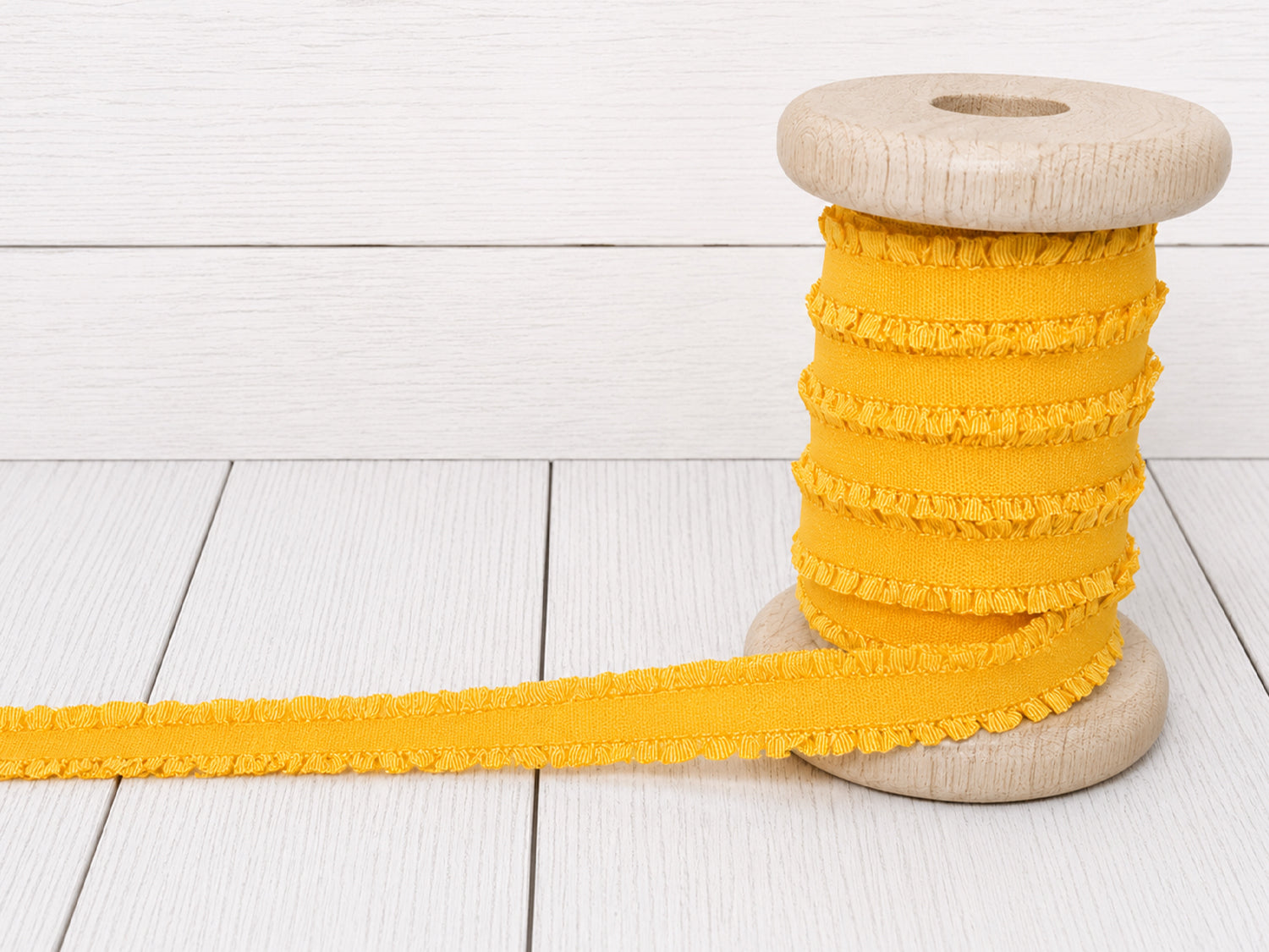 Gelbes Rüschen Gummiband auf einer Holzspule, ideal für Nähprojekte und Verzierungen.