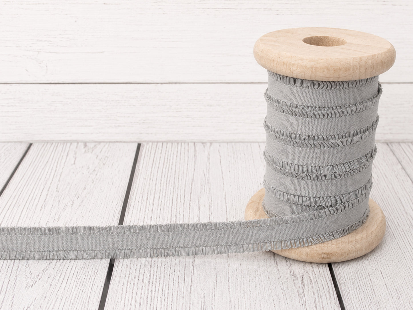 Rüschen Gummiband - hellgrau auf einer Holzspule, ideal für Nähprojekte und Verzierungen.