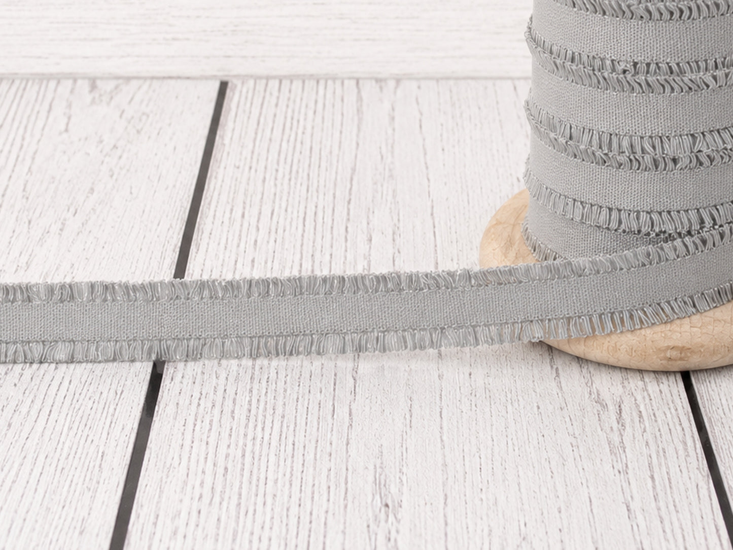 hellgrau rüschen gummiband auf einer Holzspule, ideal für Nähprojekte und Verzierungen.