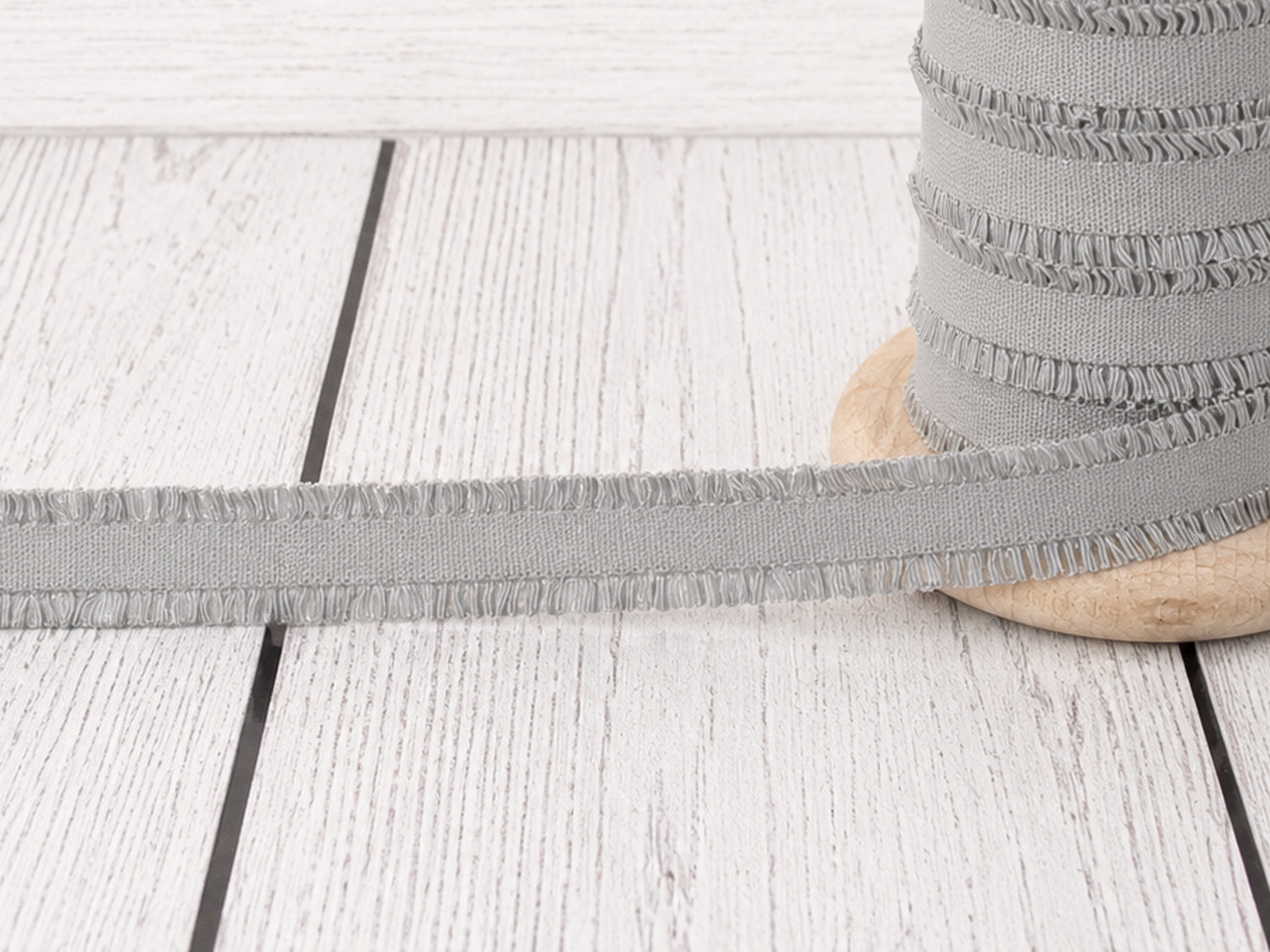 hellgrau rüschen gummiband auf einer Holzspule, ideal für Nähprojekte und Verzierungen.