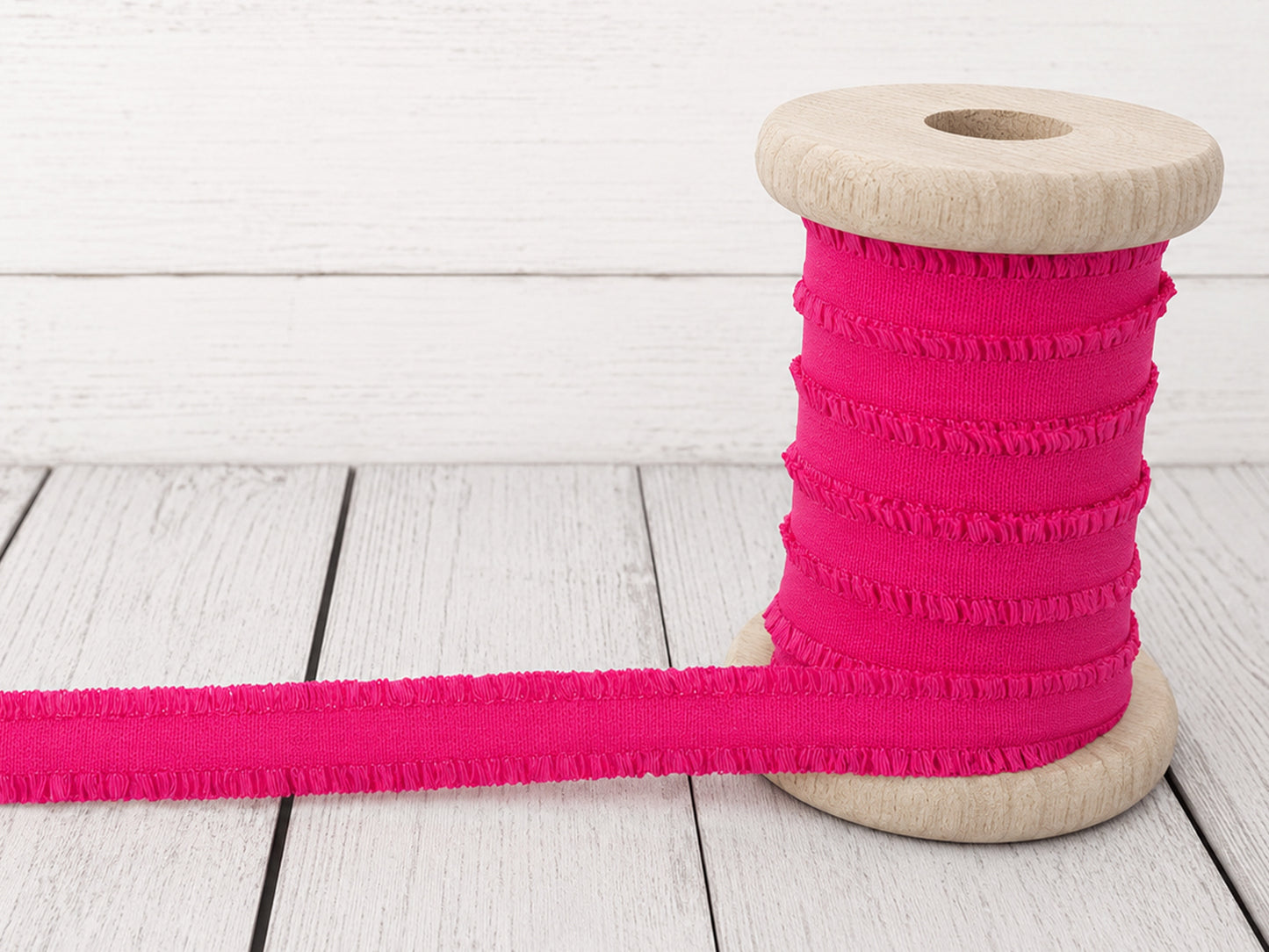 pink rüschen gummiband on a wooden spool, perfect for sewing projects and embellishments.