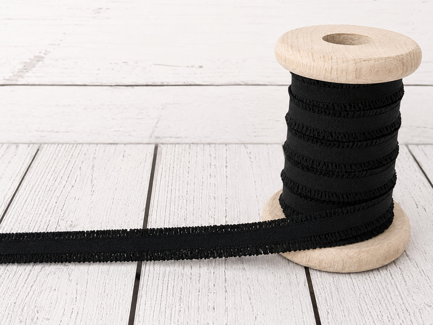 schwarzes Rüschen Gummiband auf einer Holzspule, ideal für Nähprojekte und Verzierungen.