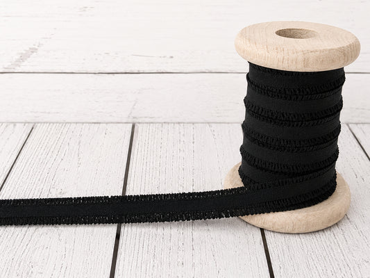 schwarzes Rüschen Gummiband auf einer Holzspule, ideal für Nähprojekte und Verzierungen.