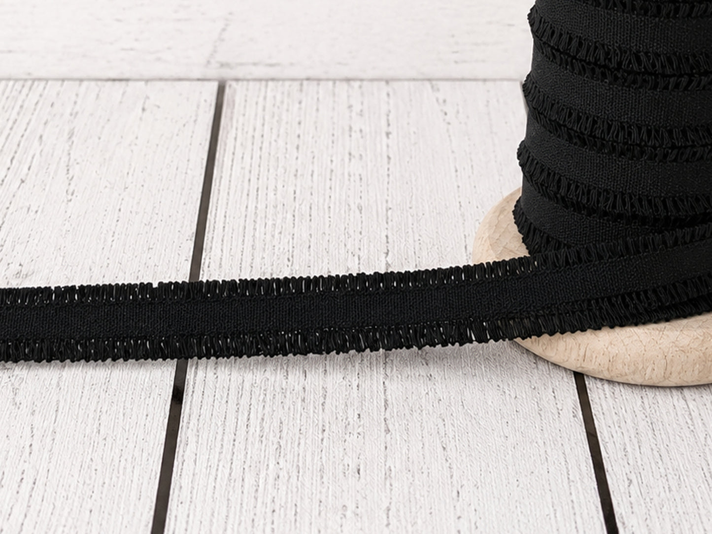 Schwarzes Rüschen Gummiband auf einer Holzspule, ideal für kreative Nähprojekte, aus 100% Polyester.