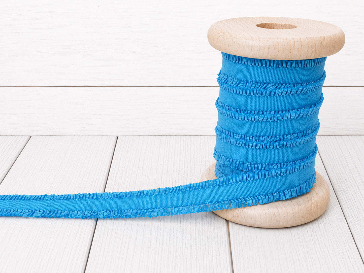 Türkises Rüschen Gummiband auf einer Holzspule für kreative Nähprojekte.