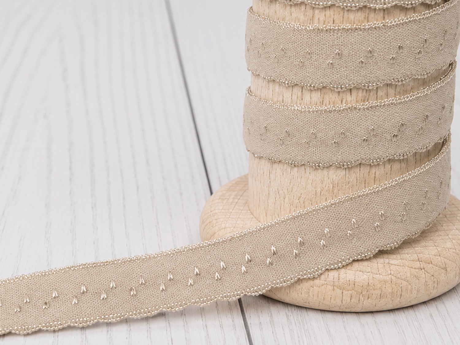 beige elastic bias tape displayed on a wooden spool with decorative scalloped edges.