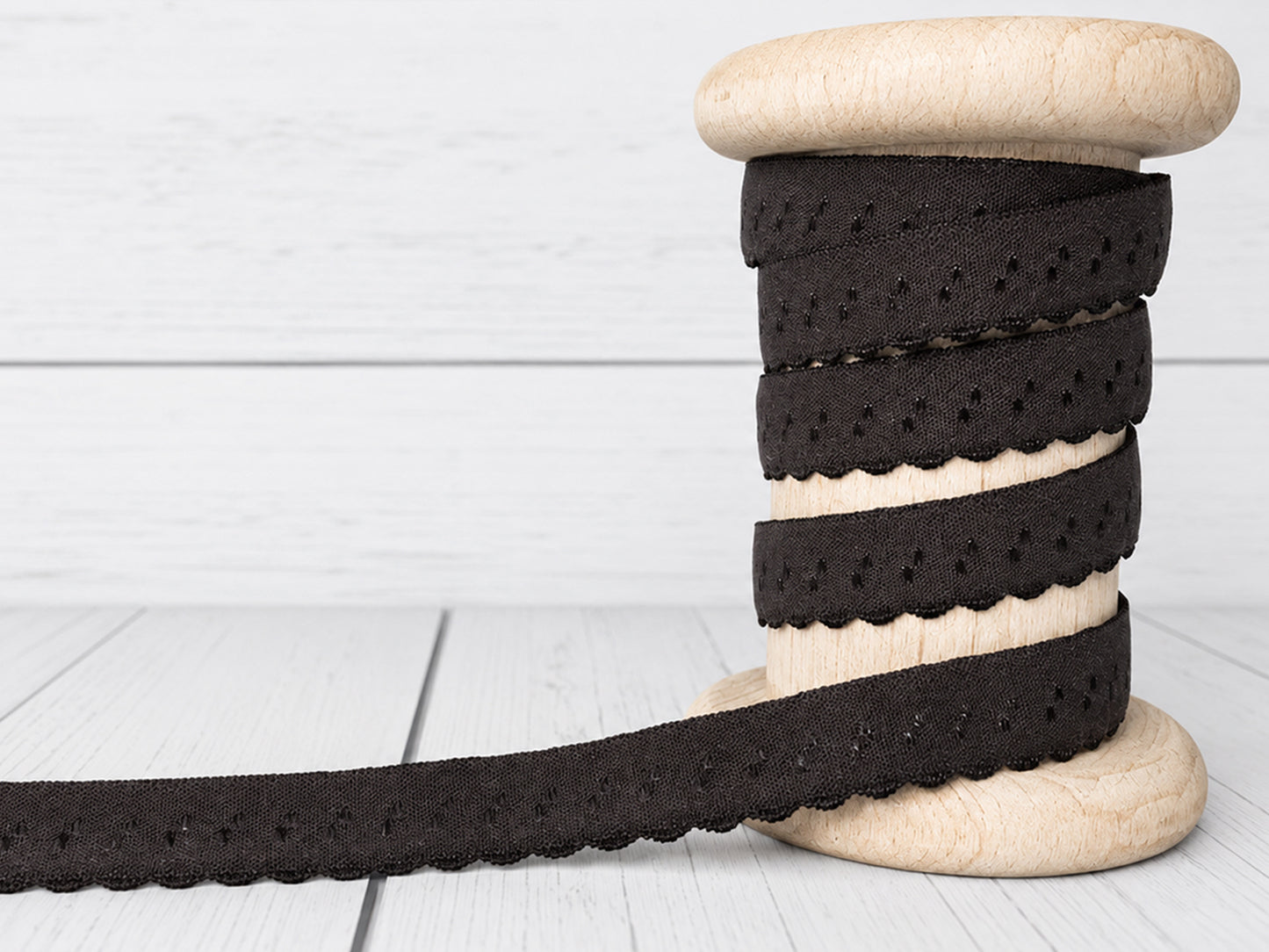 dunkelbraunes elastisches Einfassband auf einer Holzspule, mit Bogenkante und 11 mm Breite.