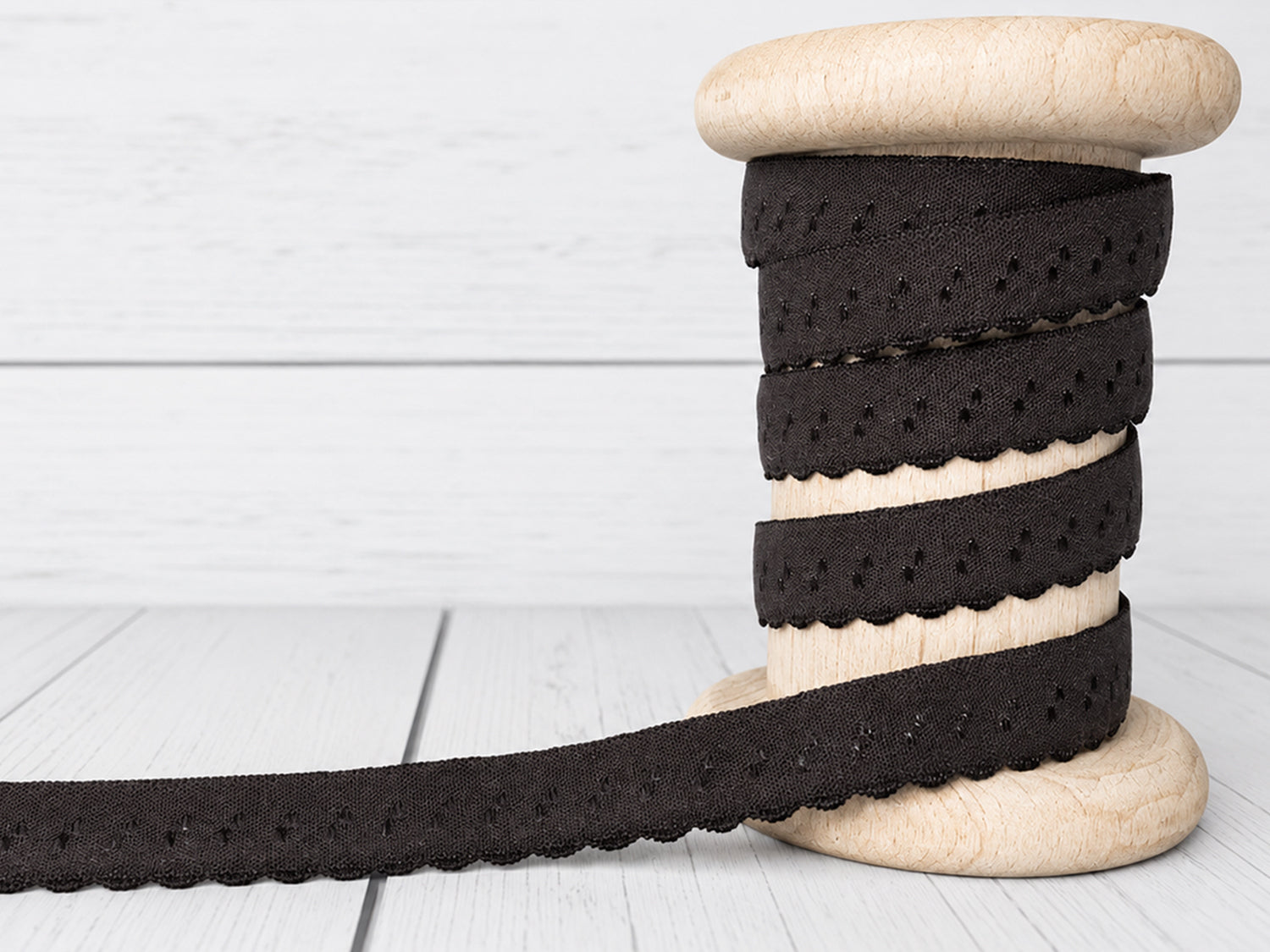 dunkelbraunes elastisches Einfassband auf einer Holzspule, mit Bogenkante und 11 mm Breite.