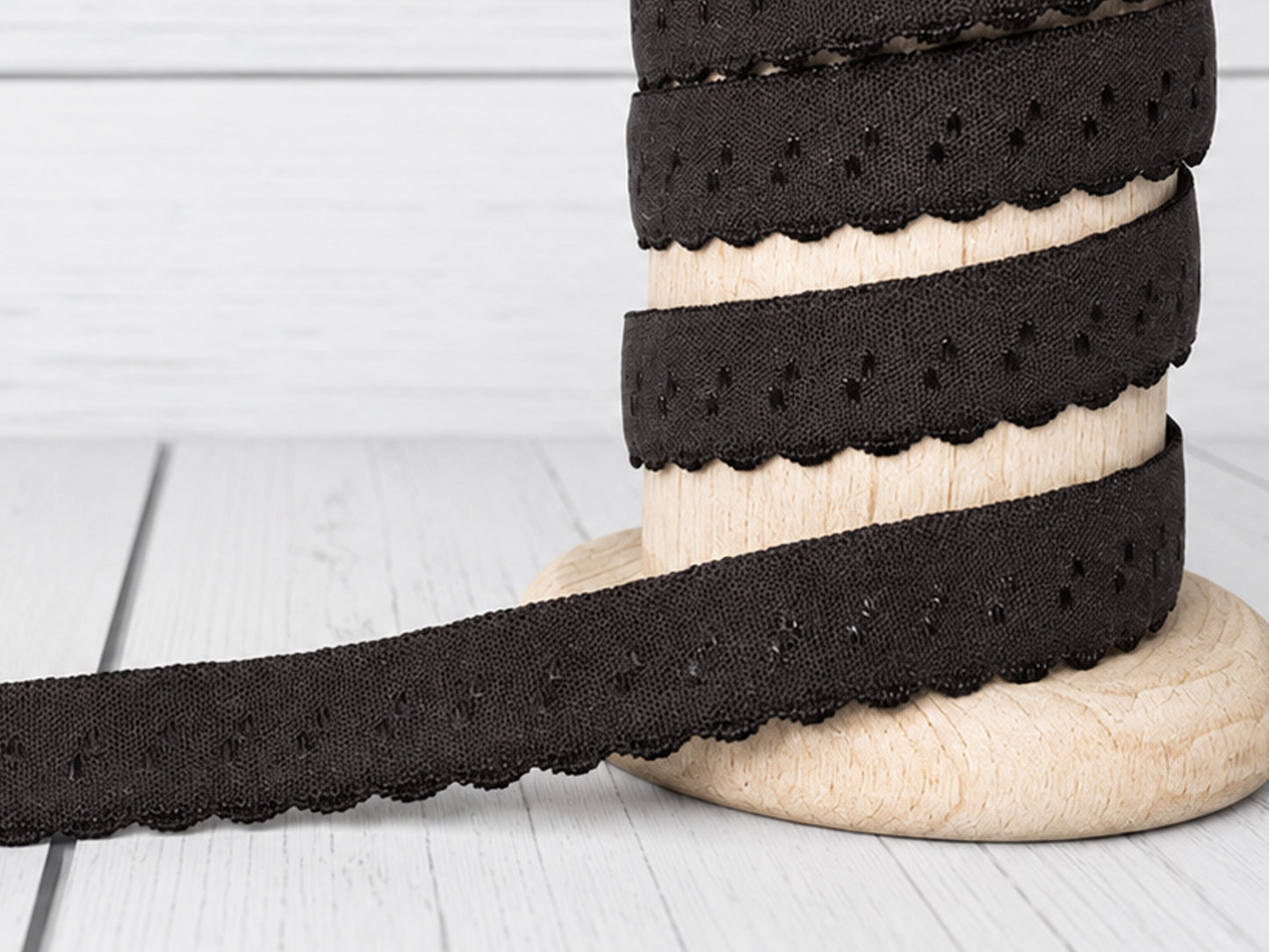 Dunkelbraunes elastisches Einfassband auf einer Holzspule, geschwungene Kante, ideal für Nähprojekte.