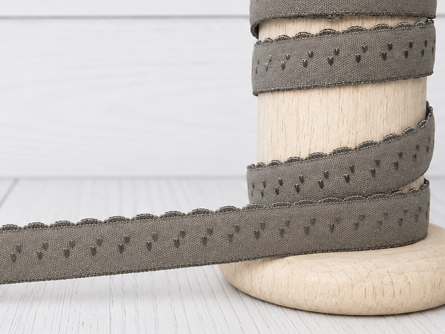 dunkles taupe elastisches Einfassband auf einer Holzspule, ideal zum Nähen und Gestalten von Textilien.