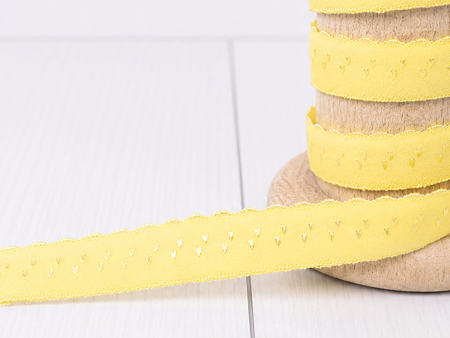 gelbes elastisches Einfassband auf einer Holzspule mit Bogenkante, ideal für kreative Projekte.