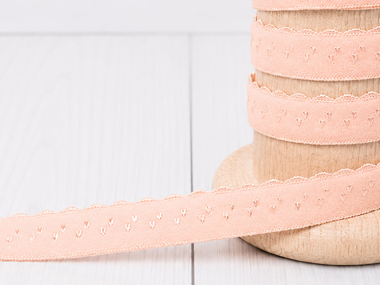 Elastisches Einfassband - lachs auf Holzspule mit Bogenkante, ideal für Nähprojekte und feine Dekoration.