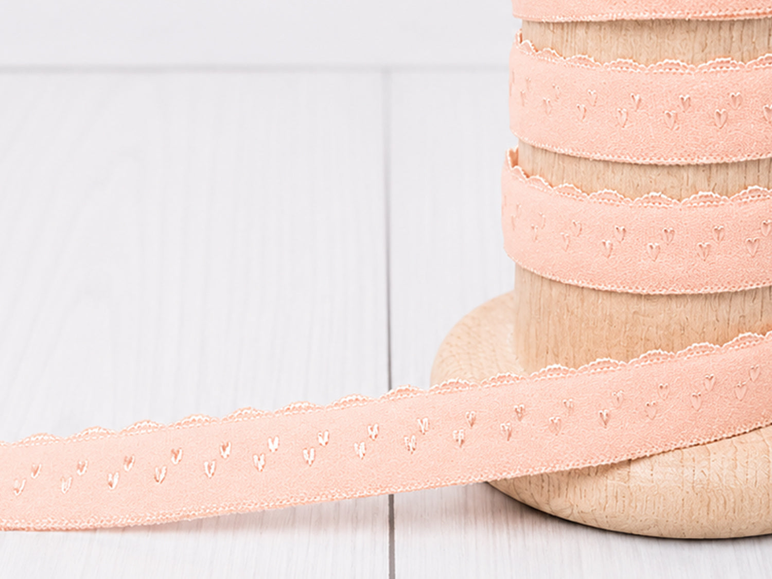 Elastisches Einfassband - lachs auf Holzspule mit Bogenkante, ideal für Nähprojekte und feine Dekoration.