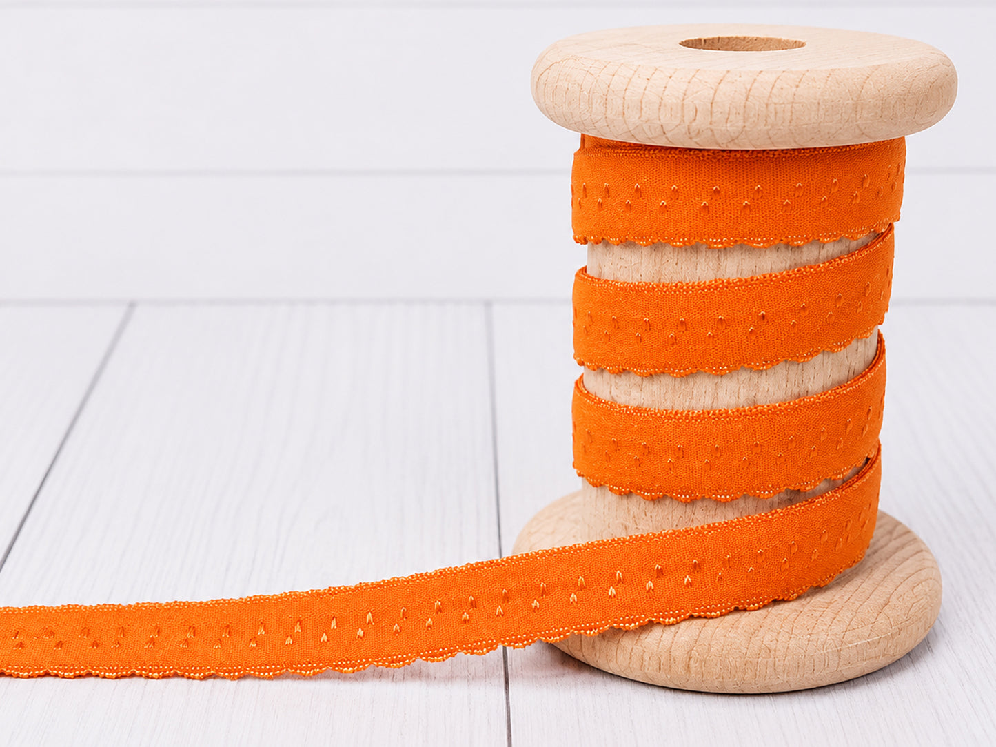 Elastisches Einfassband orange auf Holzspule, ideal für Nähprojekte und Dekoration.