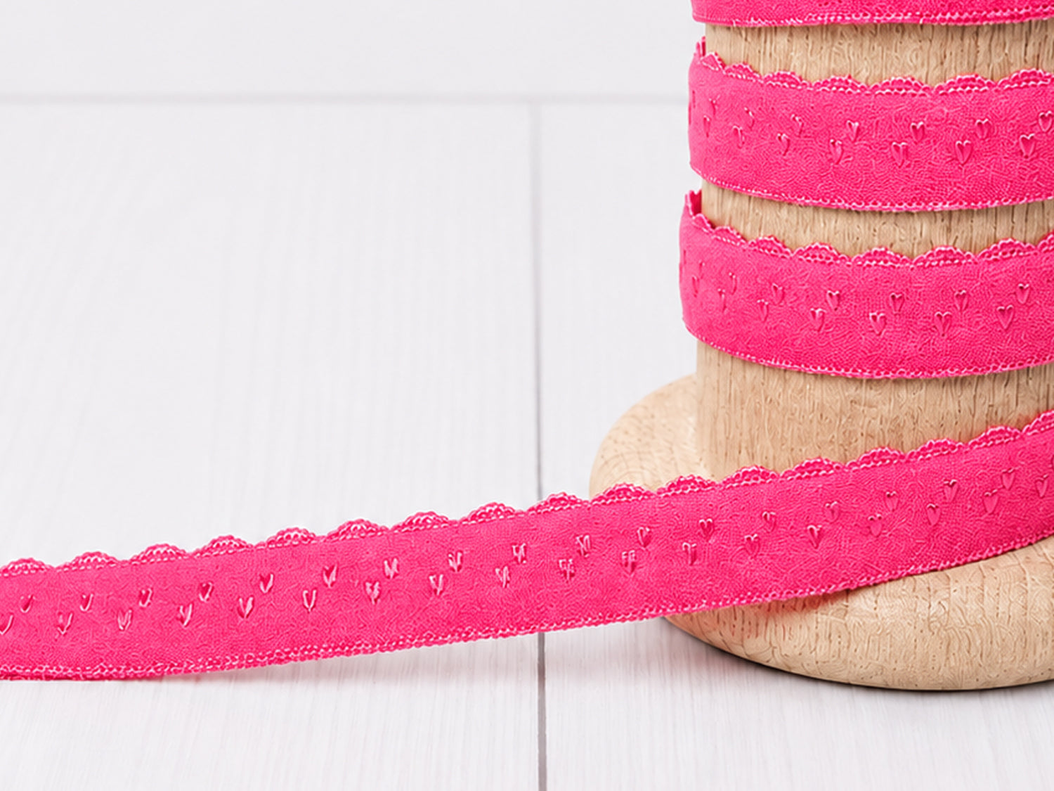 pink elastic bias tape displayed on a wooden spool, showcasing its scalloped edge design and vibrant color.