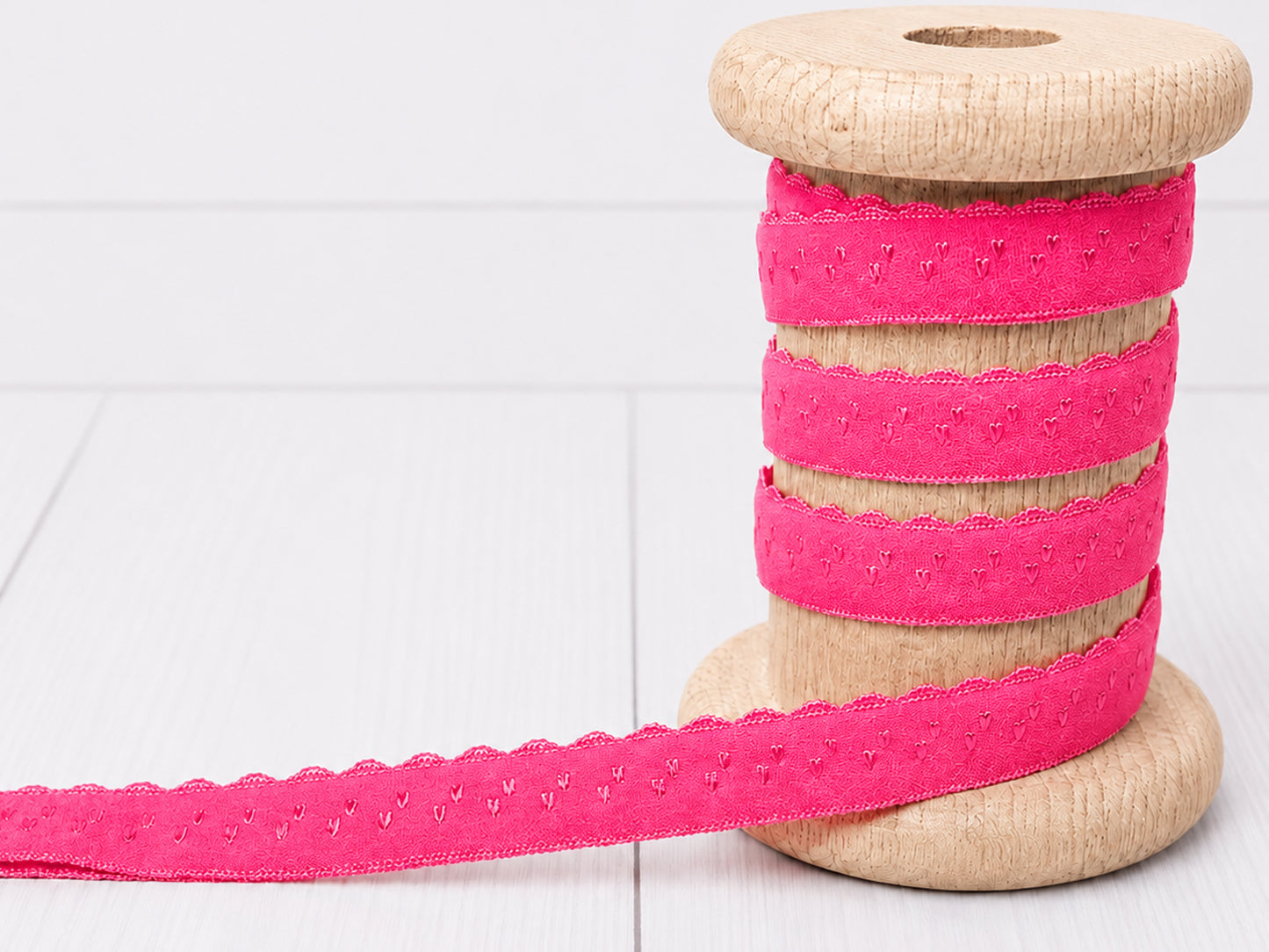 pink elastic bias tape on a wooden spool with scalloped edges, perfect for crafts and sewing projects.