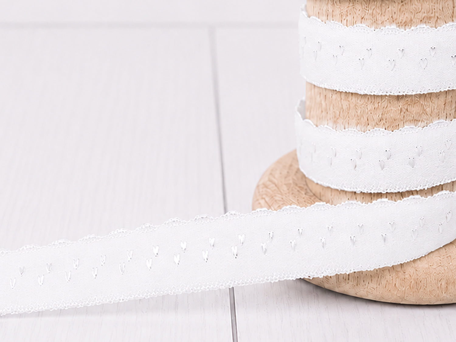 Elastisches Einfassband - weiß auf Holzspule mit Bogenkante, perfekt für kreative Nähprojekte.