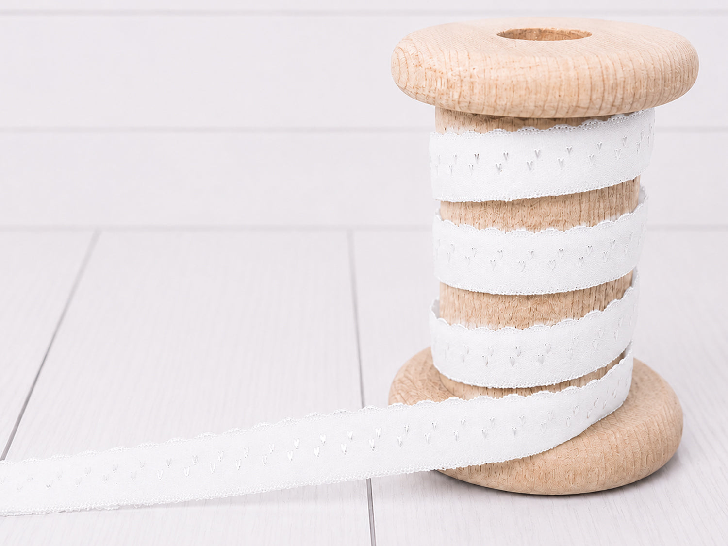 Elastisches Einfassband - weiß auf einer Holzspule, ideal für kreative Nähprojekte.