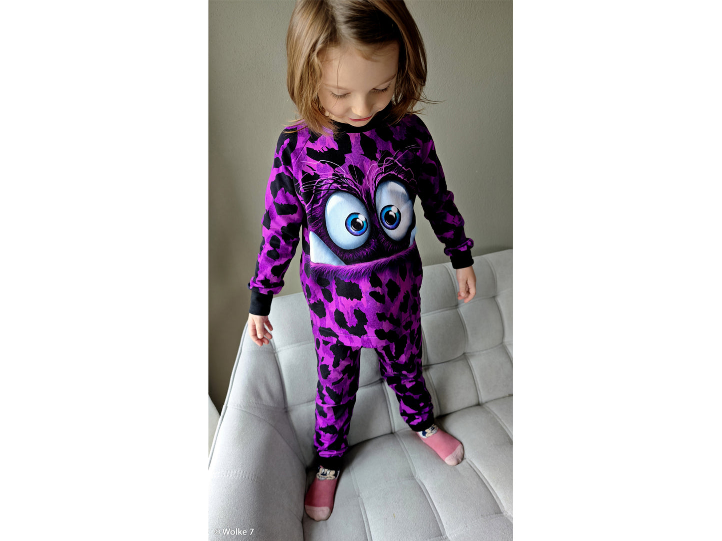 Child in a purple leopard print onesie featuring a cute monster face design.