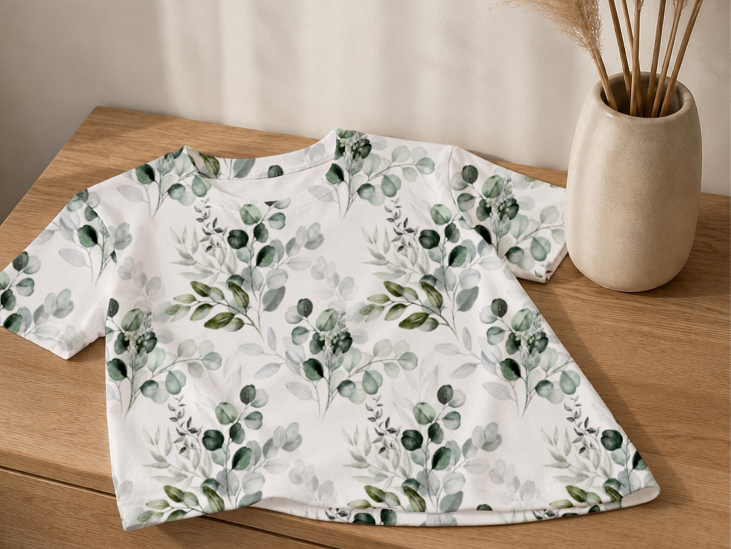 Eucalyptus leaves jersey fabric t-shirt on a wooden table with a vase and dried flowers.
