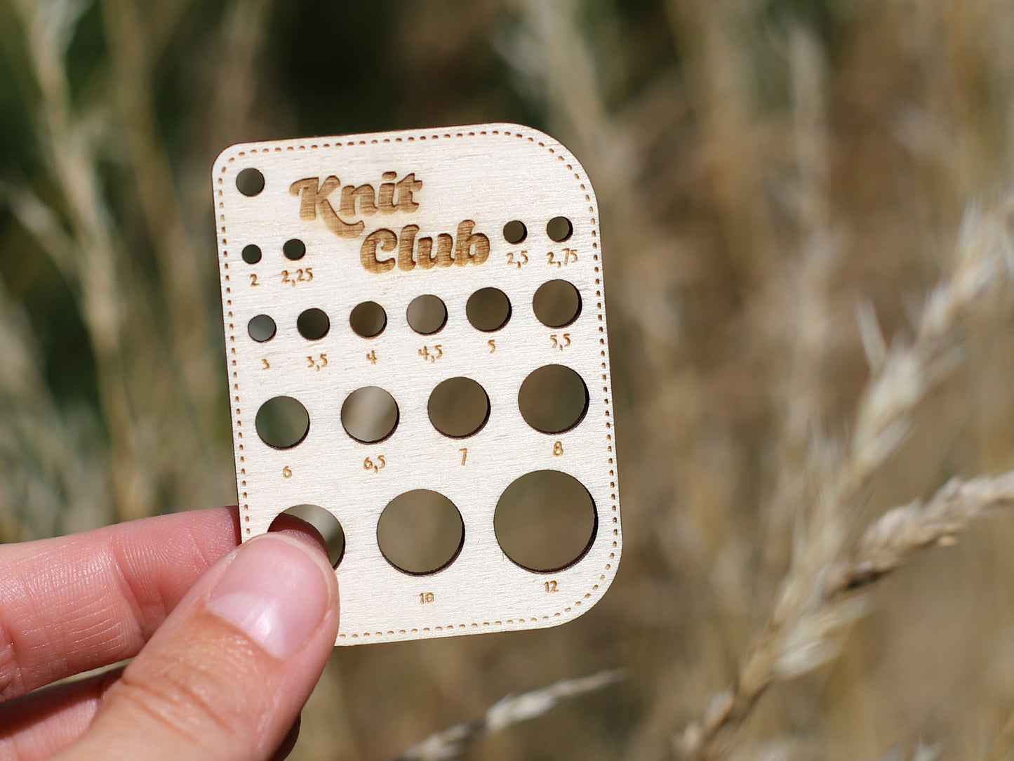 Wooden needle size gauge held in hand, featuring multiple sizes for knitting accuracy, perfect for the Knit Club.