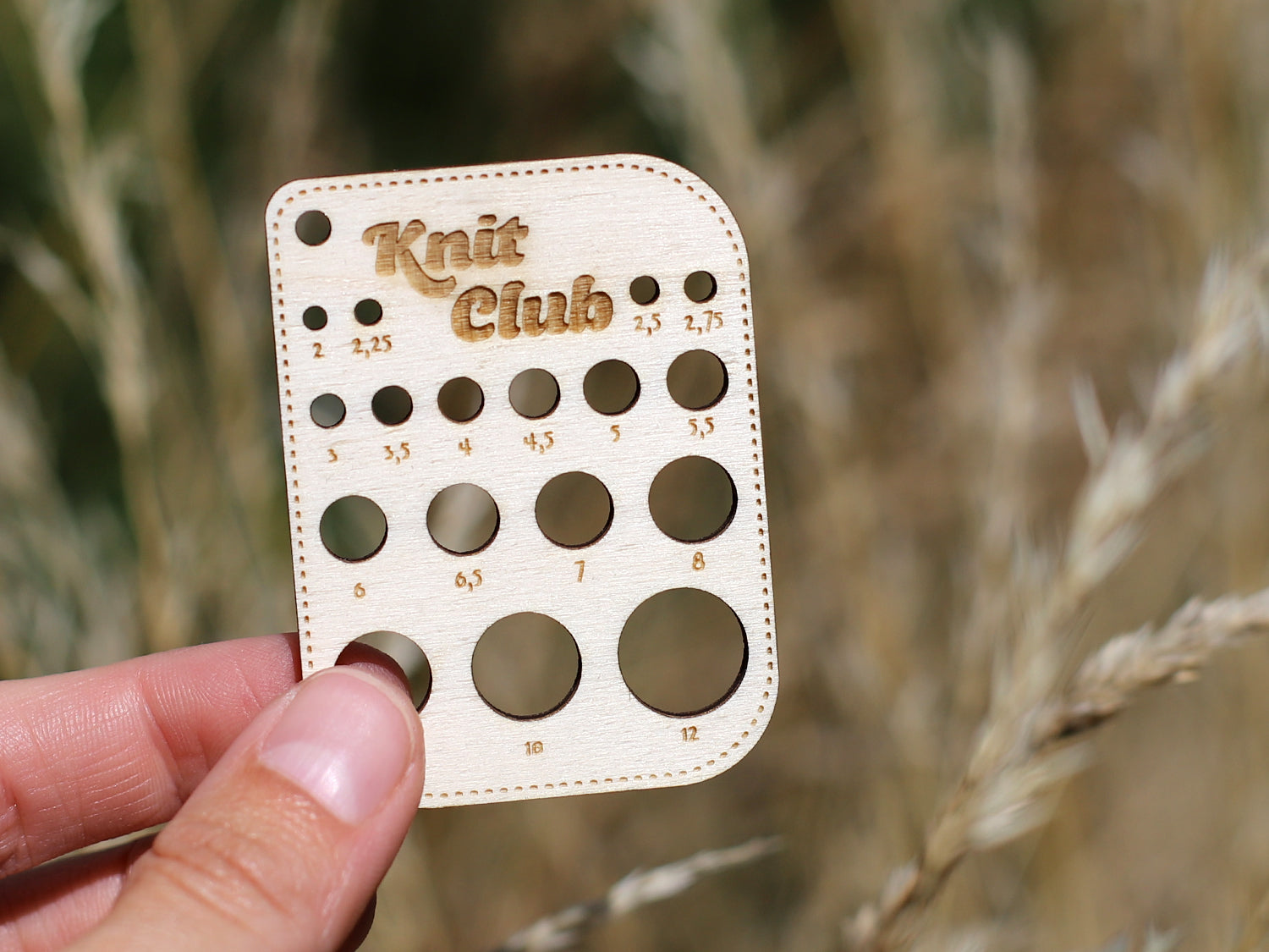 Wooden needle size gauge held in hand, featuring multiple sizes for knitting accuracy, perfect for the Knit Club.